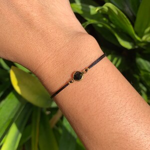 May include: A black string bracelet with a small, round, black gemstone charm.