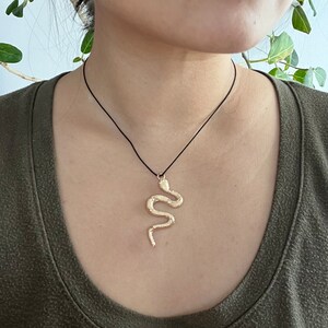 May include: A gold snake pendant necklace on a black cord. The snake is curled in a realistic pose.