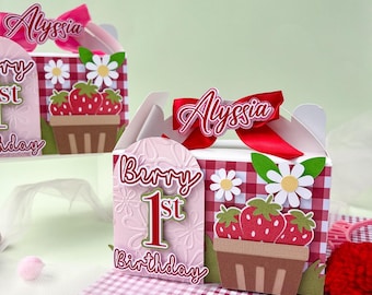 May include: A red and white gingham patterned box with a red ribbon and the name "Alyssa" on it. The box has a pink and white background with the words "Berry 1st Birthday" and a picture of strawberries in a basket.