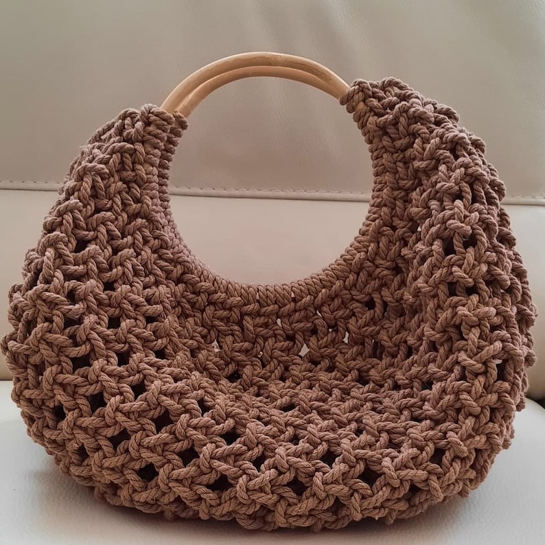 May include: A brown crocheted tote bag with a wooden handle. The bag is made of a thick, rope-like material and has a  distinctive open weave pattern.