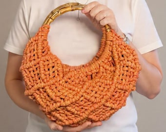 May include: A bright orange macrame handbag featuring a textured, knotted cord pattern and a curved, natural bamboo handle. The bag has a crescent-shaped silhouette with an intricate woven design throughout the body, providing a structured yet flexible appearance.