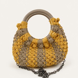 May include: A yellow and grey macrame handbag with a checkered pattern. It has a circular grey handle and a dark grey chain strap. The bag's design includes decorative knots and a rounded shape. The bag is handmade.