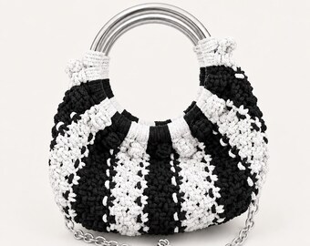 May include: A crescent-shaped handbag crafted from black and white crocheted yarn in a vertical striped pattern. The bag features a circular silver-toned metal handle at the top and a detachable silver-toned metal chain shoulder strap.