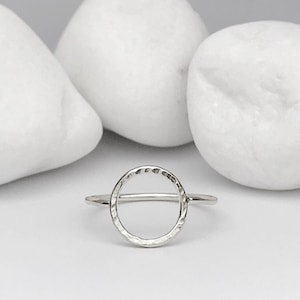 Könnte beinhalten: Ein silberner Ring mit einem gehämmerten, kreisförmigen Design. Der Ring ist schlicht und minimalistisch.