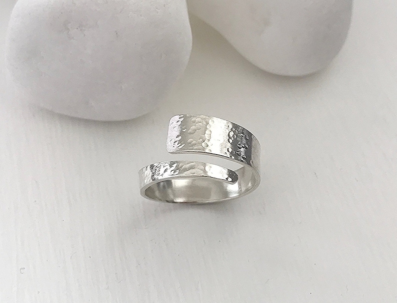 May include: A silver hammered ring with a unique open design. The ring is made from a single piece of metal that is bent into a circle and then hammered to create a textured surface.