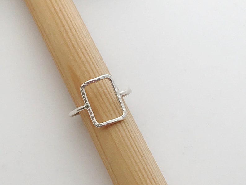 May include: A silver ring with a textured, rectangular shape. The ring is open on one side and closed on the other.