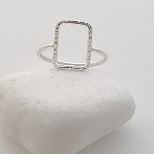 May include: A silver ring with a textured, rectangular frame.