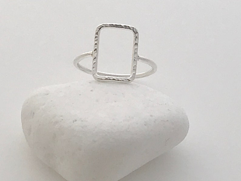 May include: A silver ring with a textured, rectangular frame.