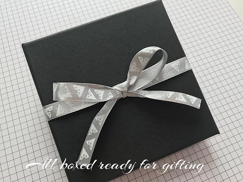 May include: A black gift box with a silver ribbon tied in a bow. The ribbon has a white geometric pattern. The text "All boxed ready for gifting" is written on the bottom of the image.