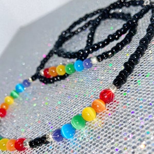 May include: A necklace with a rainbow of coloured round beads. The necklace has a black beaded chain and silver-coloured accents. The rainbow beads transition from red to orange, yellow, green, blue, and purple.