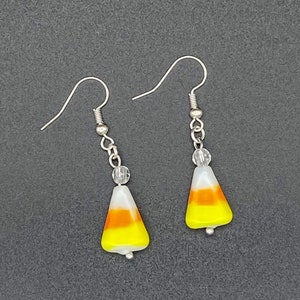 May include: A pair of silver dangle earrings with a white, orange, and yellow candy corn charm and a clear crystal bead.