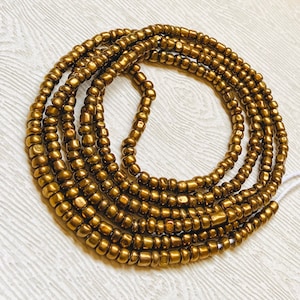 May include: A gold beaded waist chain with multiple strands of beads. The chain is made of small, round beads that are all the same size. The chain is lying on a white surface.