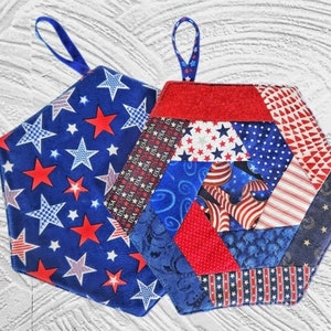 May include: Two red, white, and blue quilted pot holders with hanging loops. The pot holders are hexagonal in shape and feature a variety of patriotic patterns.