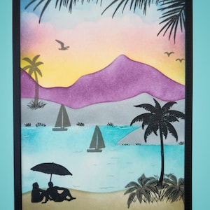 May include: A rectangular art print featuring a beach scene with a sunset sky in shades of pink, orange, and yellow. The foreground shows a sandy beach with two figures under an umbrella, palm trees, sailboats on blue water, and purple mountains.