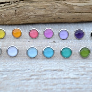 May include: Assortment of 12 colourful round stud earrings. The earrings are made of stainless steel and have a variety of colours, including yellow, orange, pink, purple, blue, green, and black.