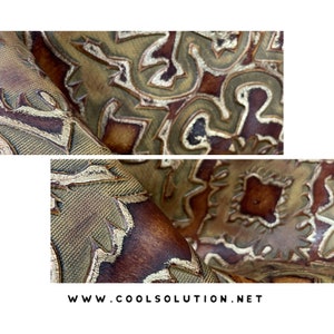May include: Close-up of a brown leather fabric with a gold embossed pattern. The fabric has a textured surface and a subtle sheen. The pattern is intricate and detailed, featuring geometric shapes and swirls. The fabric is folded in half, revealing the underside.