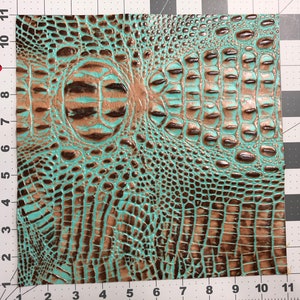 May include: A piece of turquoise and brown faux crocodile embossed leather. The leather has a textured, scaly pattern.