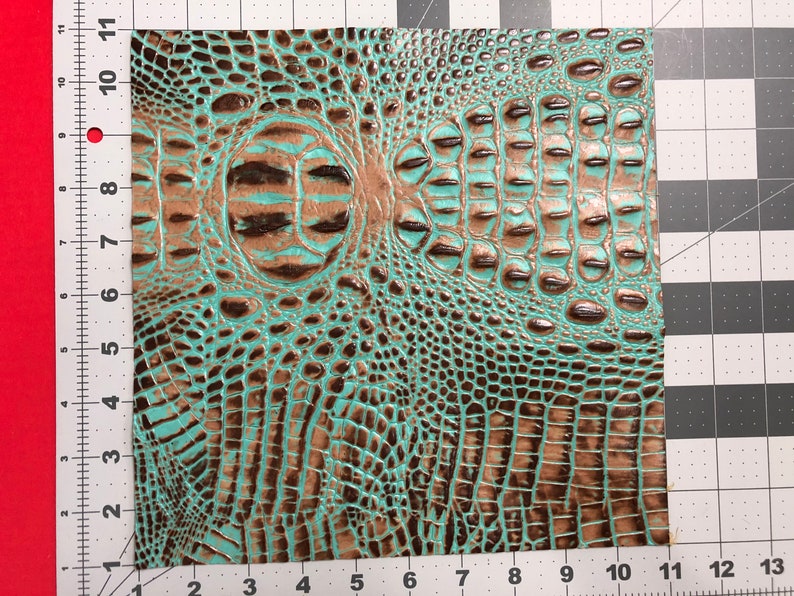 May include: A piece of turquoise and brown faux crocodile embossed leather. The leather has a textured, scaly pattern.