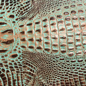 May include: Close-up of a textured, embossed leather with a crocodile skin pattern. The leather is a teal green color with brown accents.