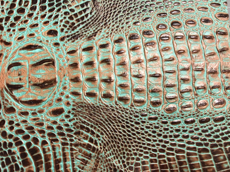 May include: Close-up of a textured, embossed leather with a crocodile skin pattern. The leather is a teal green color with brown accents.