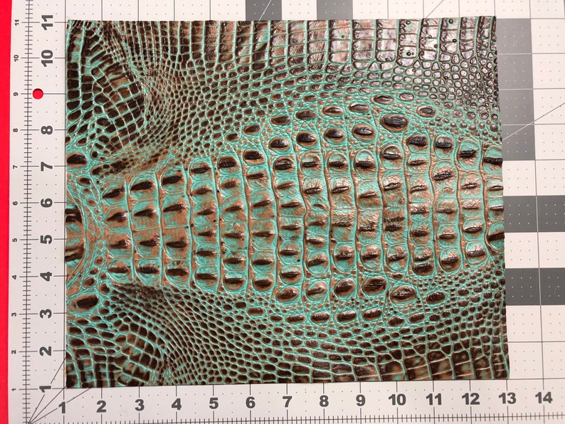 May include: Close-up of a teal and brown faux crocodile skin fabric. The fabric has a textured, embossed pattern that resembles crocodile scales.
