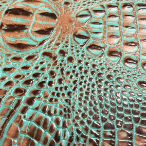 May include: Close-up of a turquoise and brown crocodile embossed leather texture. The leather has a glossy finish and a raised pattern.