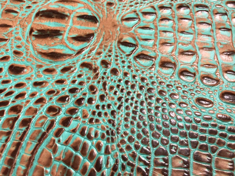 May include: Close-up of a turquoise and brown crocodile embossed leather texture. The leather has a glossy finish and a raised pattern.