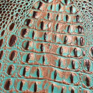 May include: Close-up of turquoise and brown faux crocodile embossed leather. The leather has a textured, scaly pattern.