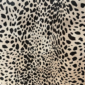 May include: Close-up of a beige fabric with a black leopard print pattern.