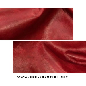 May include: Close-up of a deep red leather fabric with a textured surface. The fabric is folded and draped, showing the texture and drape of the material.