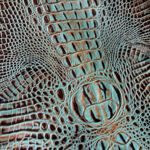 May include: Close-up of a textured turquoise and brown faux crocodile leather. The leather has a raised pattern that resembles alligator scales.