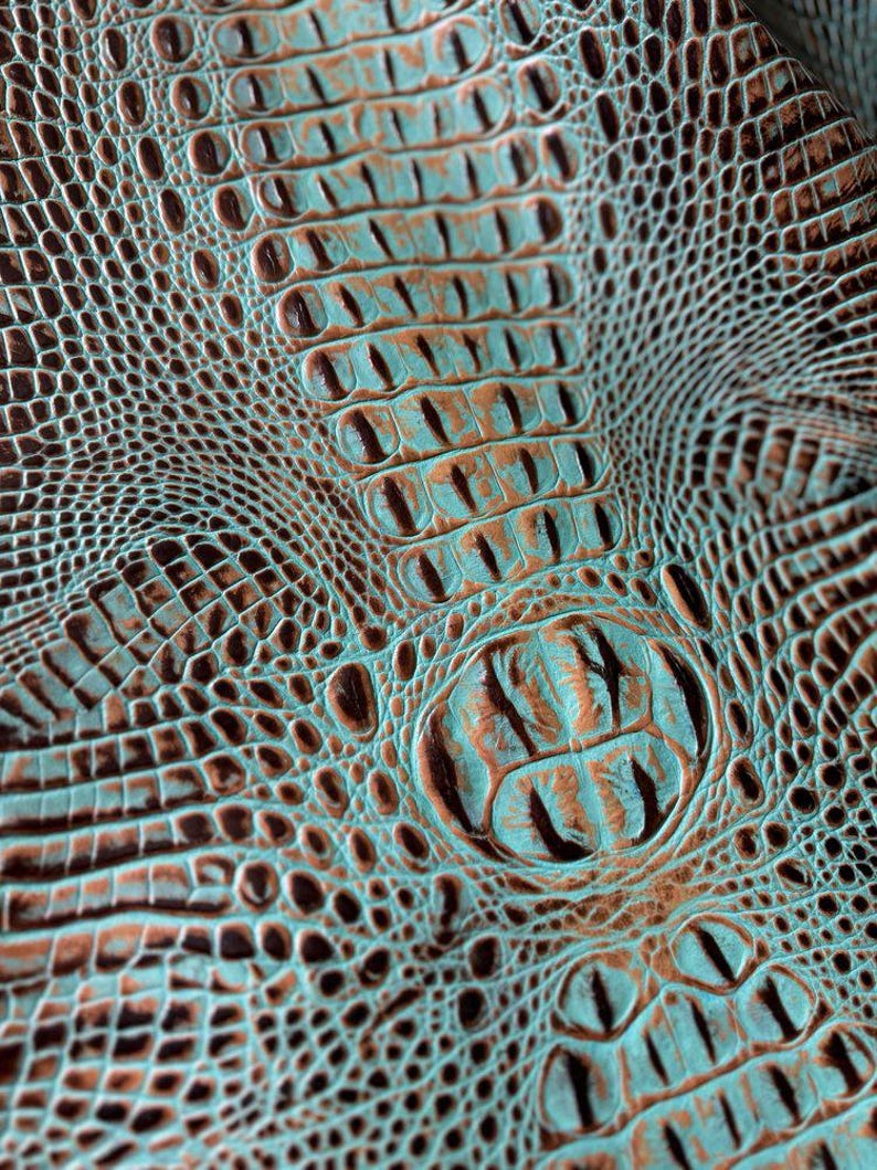 May include: Close-up of a textured turquoise and brown faux crocodile leather. The leather has a raised pattern that resembles alligator scales.