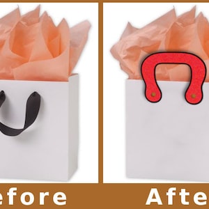 May include: A white gift bag with a black ribbon handle. The bag is filled with peach-colored tissue paper. The second image shows the same bag with a red handle.