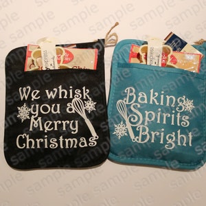 Könnte beinhalten: Zwei schwarze und blaugrüne Ofenhandschuhe aus Stoff mit weißem Text und Schneeflockenmustern. Der schwarze Handschuh sagt "We whisk you a Merry Christmas" und der blaugrüne Handschuh sagt "Baking Spirits Bright".