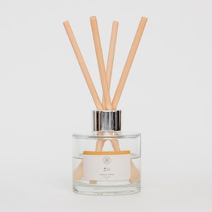 May include: A clear glass diffuser bottle with a silver collar and several light brown reeds. The bottle has a label that reads "Vanilla Truffle". The reeds are inserted into the liquid inside the bottle, a home fragrance product.