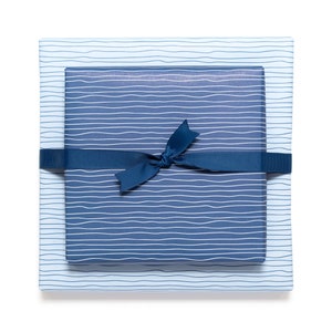May include: Two gift boxes wrapped in blue paper with white wavy lines. The top box is a darker shade of blue than the bottom box. A dark blue ribbon is tied around the boxes in a bow.