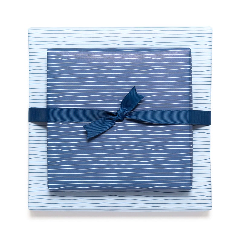 May include: Two gift boxes wrapped in blue paper with white wavy lines. The top box is a darker shade of blue than the bottom box. A dark blue ribbon is tied around the boxes in a bow.