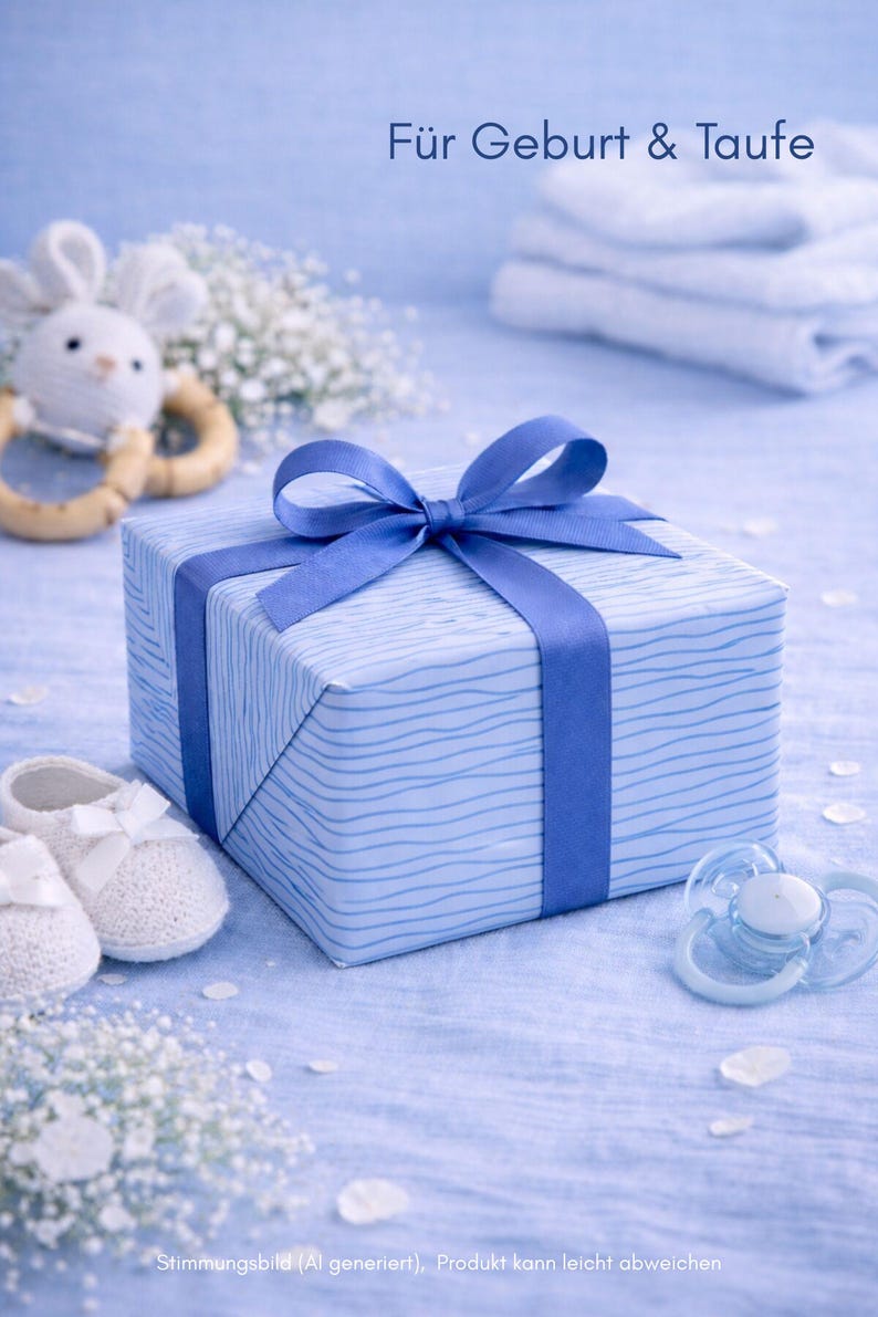 May include: A blue gift box tied with a blue ribbon, baby booties, a pacifier, and a toy bunny on a light blue surface. The gift box is wrapped in blue paper with a wavy pattern. Text in the image reads "F&uuml;r Geburt & Taufe".