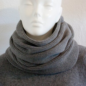 Puede incluir: Una bufanda de punto gris en forma de infinito. La bufanda es gruesa y cálida, y es perfecta para mantener el cuello caliente en invierno.