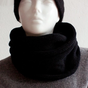 May include: A black knit infinity scarf. The scarf is folded in half and worn around the neck.