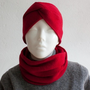 Peut inclure: Un bonnet rouge de style turban et une écharpe infinie assortie sont présentés sur un mannequin. Le bonnet est d'un rouge profond, avec un design torsadé. L'écharpe est également rouge. Le mannequin porte un pull gris.