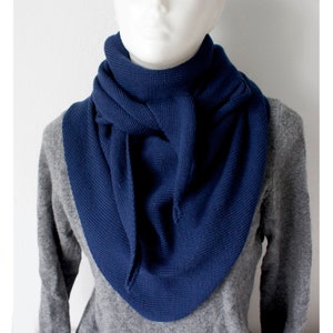 Peut inclure: Une écharpe en tricot bleu marine de forme triangulaire. L'écharpe est pliée et nouée autour du cou.