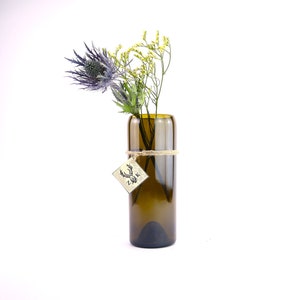 Könnte beinhalten: Eine dunkelgrüne Glasvase mit rustikalem Bindfaden um den Hals. Die Vase ist mit einem Strauß blauer Disteln und gelber Blumen gefüllt.