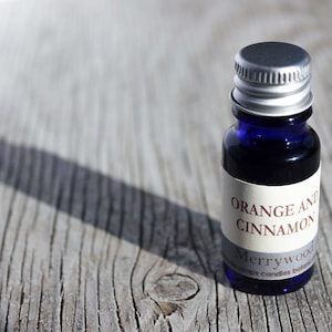 May include: A small blue glass bottle with a silver lid. The bottle has a white label with the text "Orange and Cinnamon Merrywood soaps candles bath".