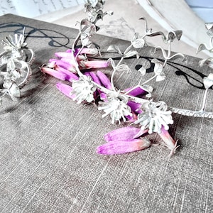 May include: A silver floral crown with delicate leaves and flowers. The crown is lying on a textured surface with pink flower petals.