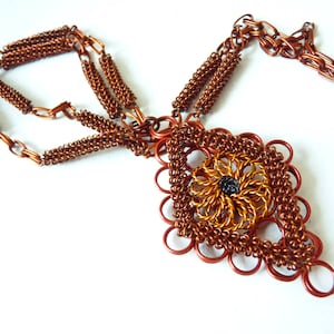 May include: A copper wire necklace with a large, intricate pendant. The pendant is made of woven copper wire and has a dark brown center.
