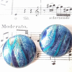 May include: A pair of blue, green, and silver swirl patterned earrings. The earrings are round and have a glossy finish.