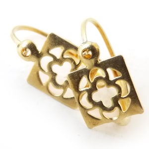 Könnte beinhalten: Ein Paar goldfarbene Ohrringe mit quadratischem Design und einem ausgeschnittenen Blumenmuster.