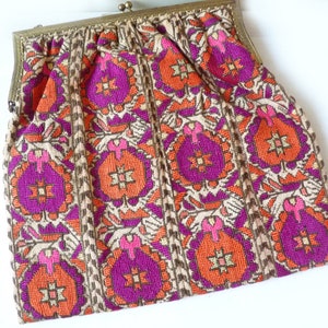 Könnte beinhalten: Eine vintage bestickte Handtasche mit einem Messingverschluss. Die Tasche hat ein geometrisches Muster in Orange-, Rosa- und Lilatönen auf einem beigefarbenen Hintergrund.