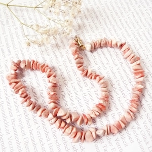 May include: A pink and white gemstone necklace made of small, irregular shaped stones. The necklace is strung on a gold chain.
